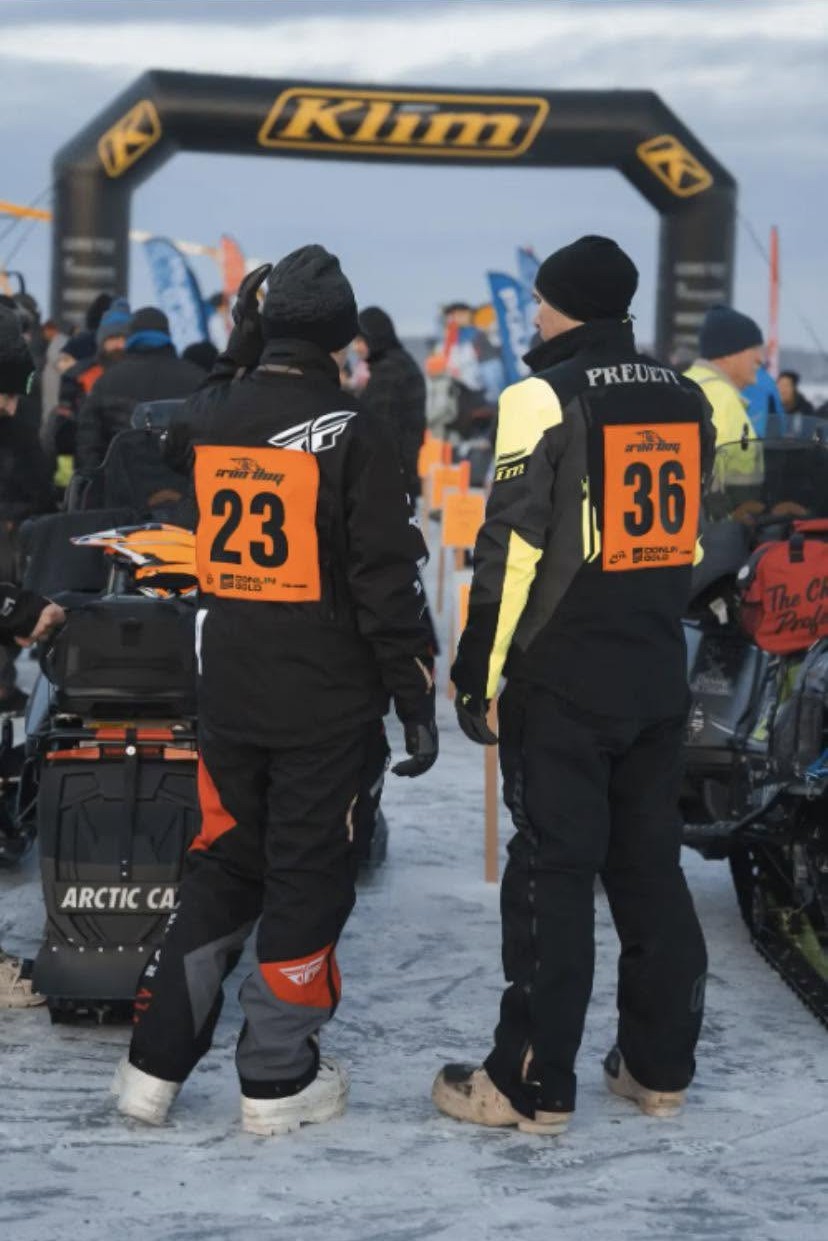 Iron Dog 2025 racers wearing custom bibs 23 and 36 under the Klim start arch
